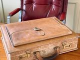 une valise marron posée sur une table en bois devant une chaise rouge