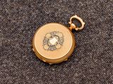 une petite montre de poche en or posée sur un tissu gris