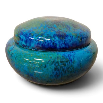 un bol bleu avec un couvercle posé sur une surface blanche