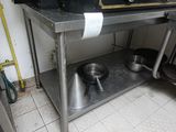 table en acier inoxydable sur laquelle sont posés des casseroles et des poêles, dans une cuisine professionnelle