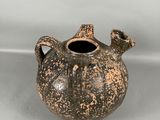 un vase noir et marron posé sur une surface blanche