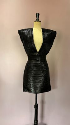 une robe en cuir noir posée sur un mannequin contre un mur blanc