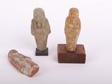 trois figurines de l'Égypte antique posées sur des socles en bois, sur une surface blanche