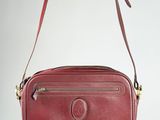 a red leather cross body bag hanging from a wall