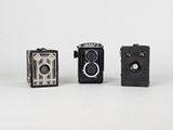 three old cameras sitting side by side on a white surface