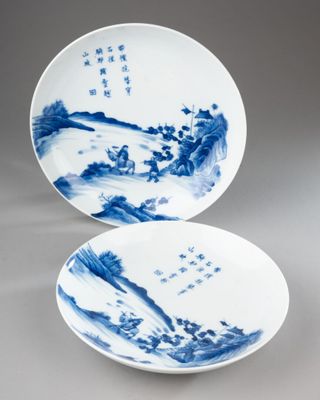 two blue and white plates with designs of mountains and trees on them