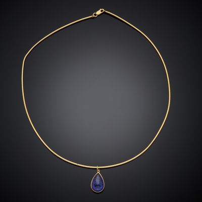 a gold necklace with a blue stone pendant on a black background