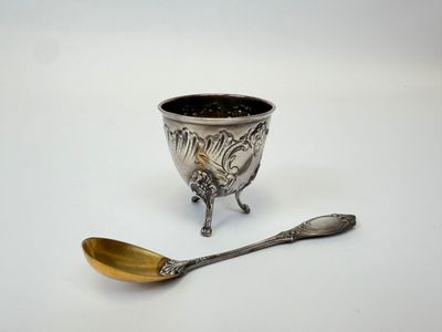 une tasse en argent et une cuillère posées sur une surface blanche