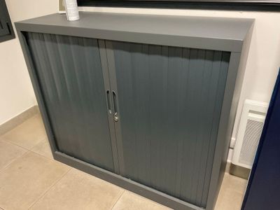 une armoire en métal gris dans une salle de bains, avec un miroir accroché au mur