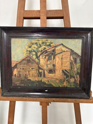 tableau représentant une vieille maison posée sur un chevalet devant un mur blanc