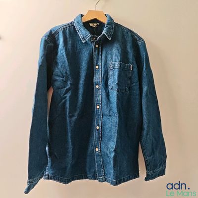denim shirt hanging on a hanger on a white wall