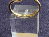 bague plaquée or ornée d'une perle blanche sur un socle en acrylique transparent