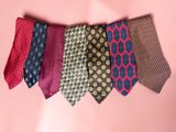 several different colored ties hanging from a line on a pink background