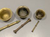 three brass bowls and two brass screws on a white surface