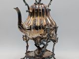 une théière ancienne en argent posée sur un socle, sur fond gris