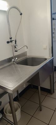 un évier en inox dans une cuisine, avec un réfrigérateur en arrière-plan