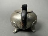 a small silver pot with a black handle on a table