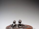 une sculpture en bronze représentant deux enfants assis sur un socle circulaire