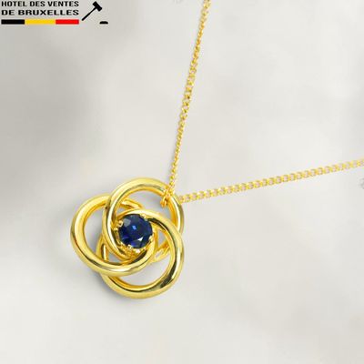 a close up of a gold necklace with a blue stone in the center