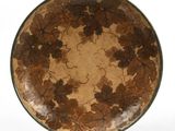 une assiette marron et verte décorée de feuilles, posée sur une surface blanche