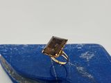 une image représentant une bague en or sertie d'un quartz fumé sur une pierre bleue