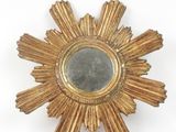 a gold starburst shaped mirror on a white wall