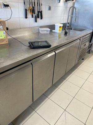 un plan de travail en acier inoxydable dans une cuisine professionnelle, avec de nombreux ustensiles accrochés au mur