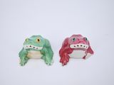 deux figurines représentant une grenouille et une autre grenouille, posées sur un fond blanc