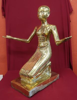 statue d'une femme vêtue d'une robe dorée, assise sur un socle rouge