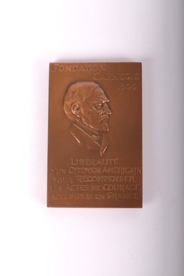 La plaque se trouve sur le mur d'un immeuble où est représenté un homme en costume-cravate.