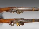 two pistols with wooden grips and brass fittings on a white background