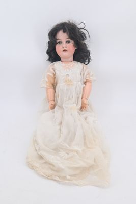 an old doll with black hair and a white dress sitting on a white surface