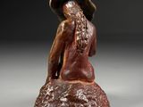 bronze statue of a woman sitting on a rock wearing a hat