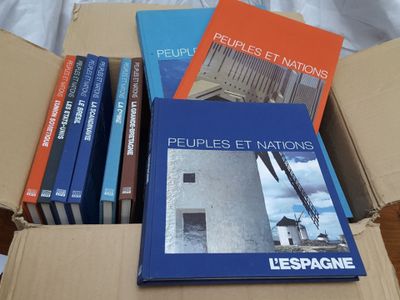 several books in a cardboard box on a bed with a white sheet