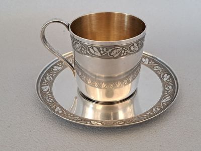 a silver cup and saucer sitting on a saucer