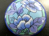 des fleurs violettes et bleues sur un fond bleu et vert, sur un bouton