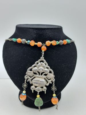un collier avec un pendentif en argent et des perles orange sur un mannequin noir