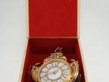 une horloge dorée dans un coffret rouge posé sur une surface blanche