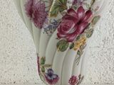 a white vase with pink flowers on it sitting on a table
