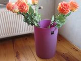 un vase violet contenant des roses orange, posé sur un parquet