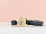 un gros plan d'une montre posée sur une surface blanche, avec un fond rose