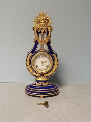 a blue and gold clock on a stand with a key