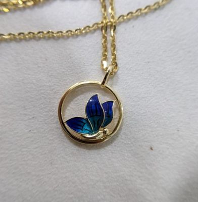 a close up of a gold necklace with a blue flower on it