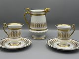 trois tasses à café blanches et dorées avec leurs soucoupes, posées sur une table
