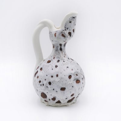 a white vase with brown spots on it on a white surface