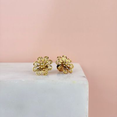 une paire de boucles d'oreilles en forme de fleurs en or posées sur un bloc de marbre