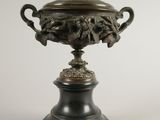 une urne en bronze posée sur un socle noir, sur fond blanc