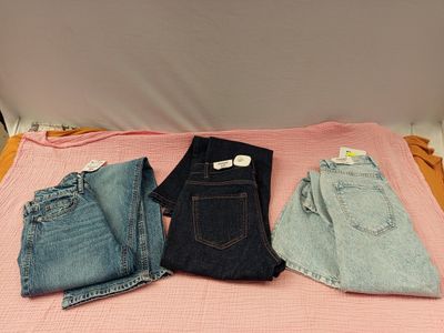 trois paires de jeans disposées sur un lit recouvert d'une couverture rose