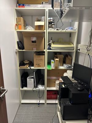 a room with a computer, printer, and other items on the shelves