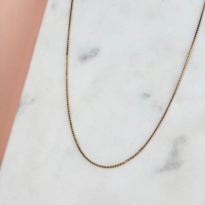 un collier à chaîne en or posé sur une surface en marbre